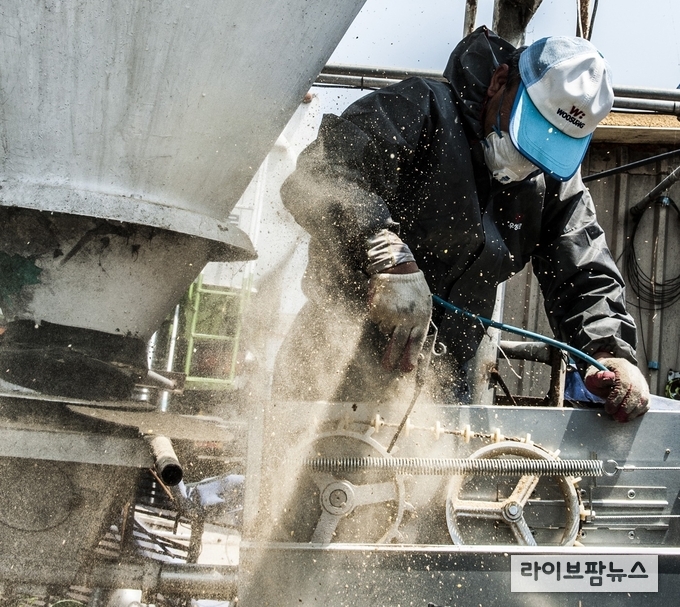 사료 배송 기사가 농장에 도착하여 사료 이송 라인을 에어브러쉬로 청소하고 있다.